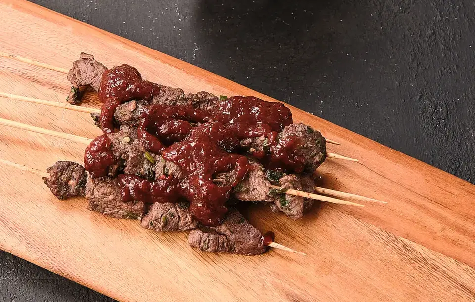 Beef skewers with strawberry jalapeño spread on a wooden serving board