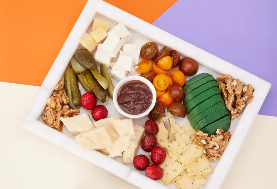 Cheese board with strawberries, tomatoes, pickles, walnuts, and strawberry jalapeño spread