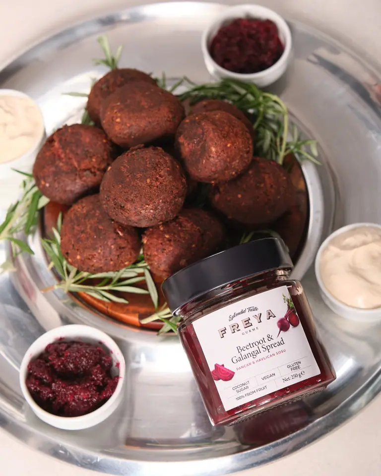 Beet and galangal falafel on greens with small bowls of dip